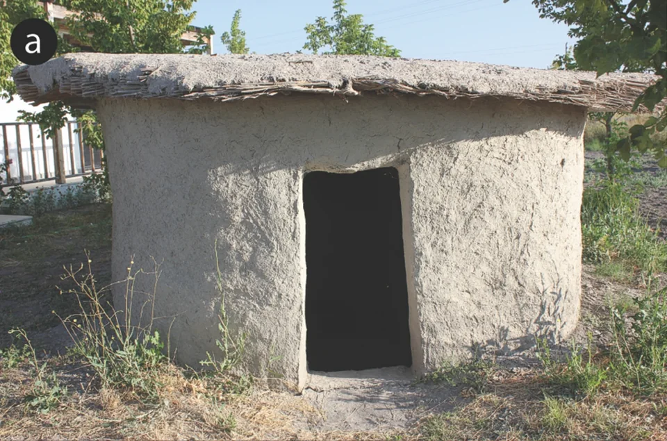 Low mud-brick replica house with a reed roof and dark doorway